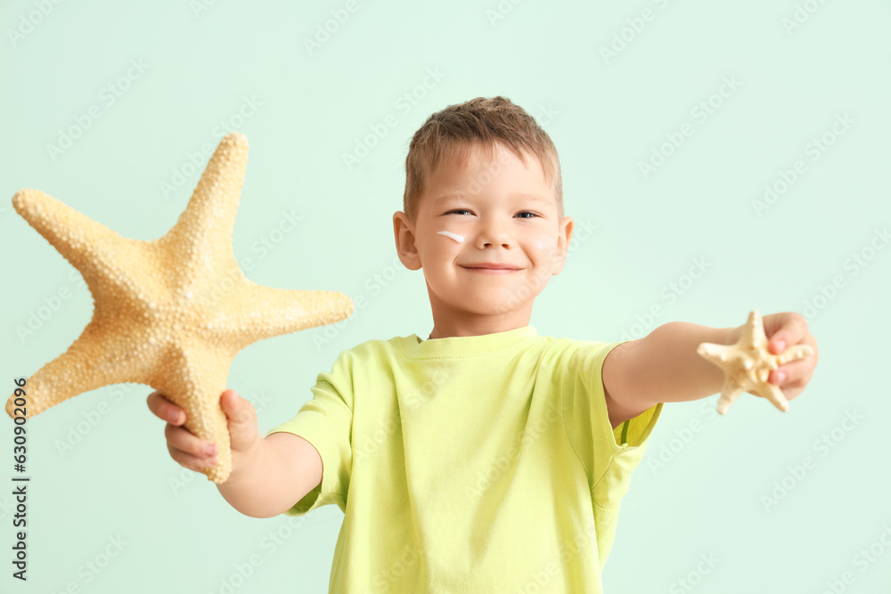 Little boy with starfishes and sunscreen cream on his face against pale green background