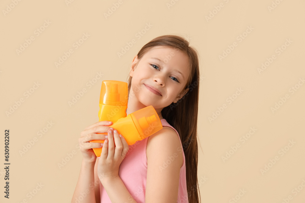 Little girl with bottles of sunscreen cream on beige background