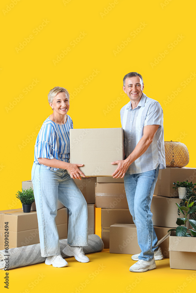 Mature couple carrying moving box on yellow background