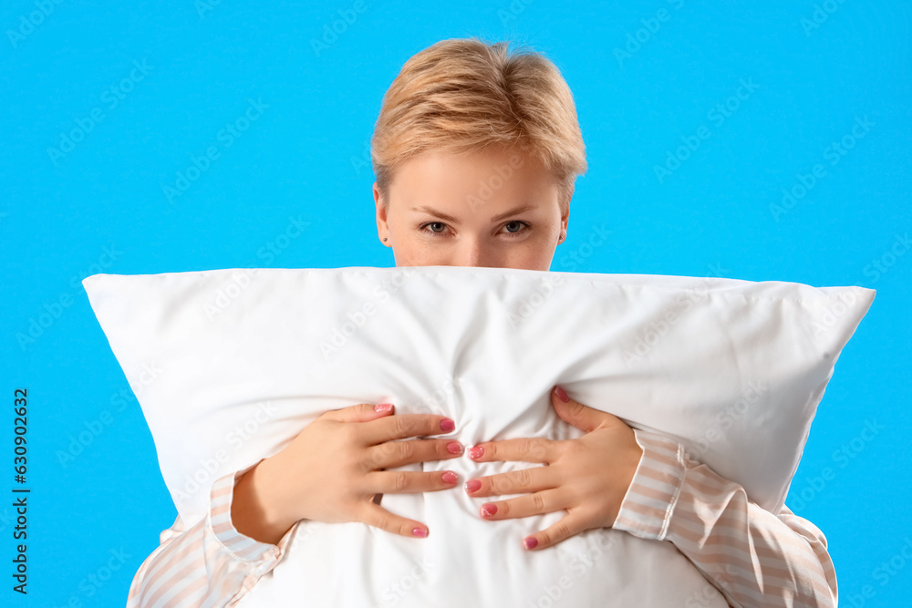 Young woman in pajamas with pillow on blue background