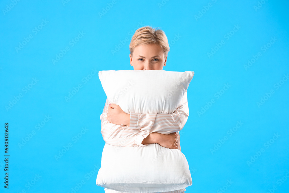 Young woman in pajamas with pillow on blue background