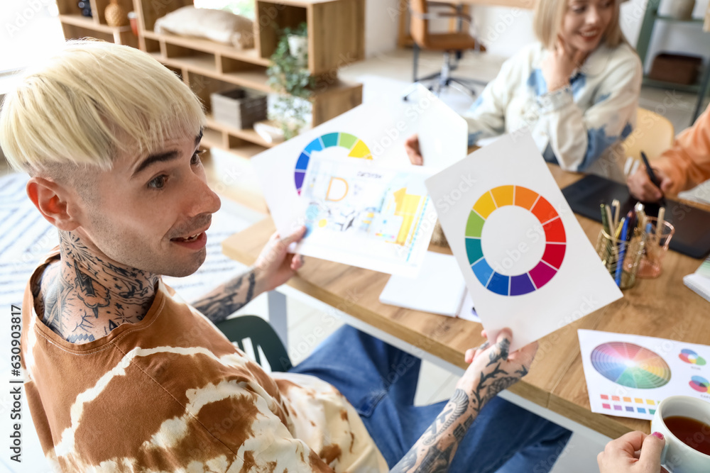 Male graphic designer working with co-workers at table in office, closeup