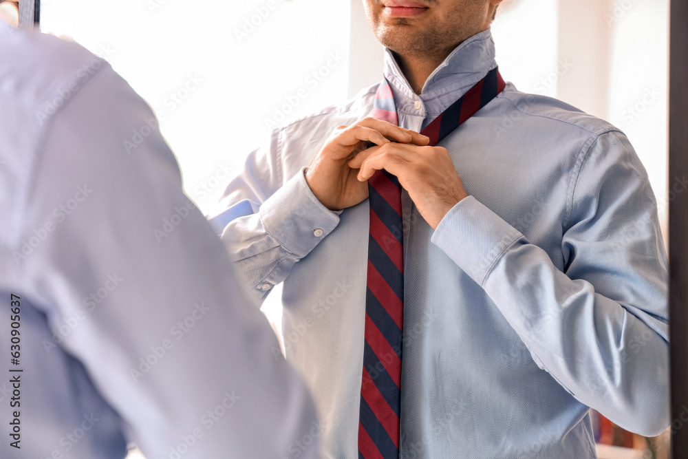 Young businessman tying his necktie in front of mirror at home, closeup