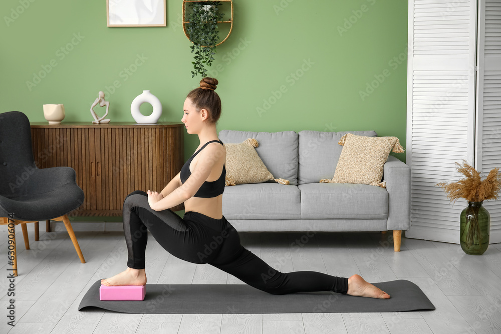 Sporty young woman practicing yoga with block at home