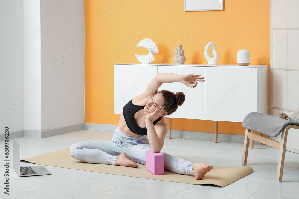 Sporty young woman practicing yoga with block at home