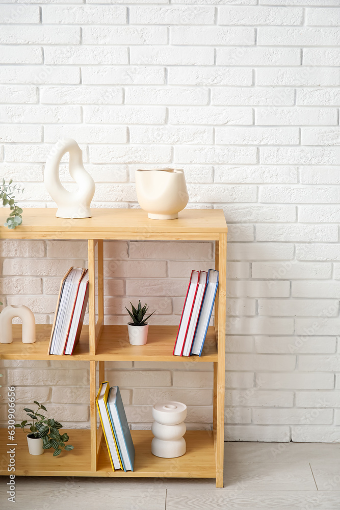 Bookshelf with houseplants near white brick wall in room