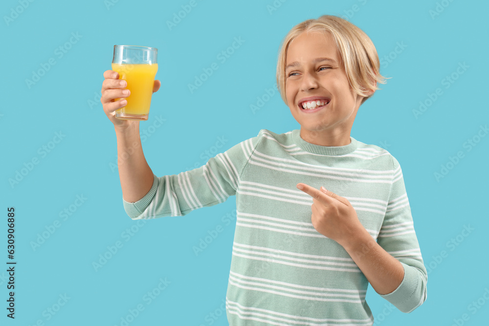 Little boy pointing at glass of orange juice on blue background