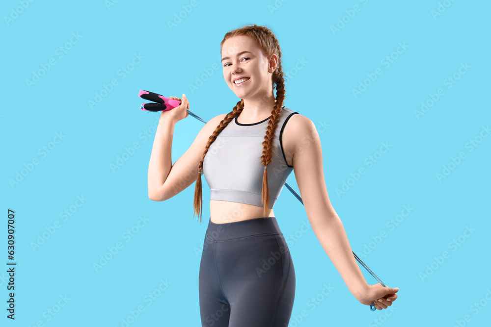 Sporty young woman with skipping rope on blue background