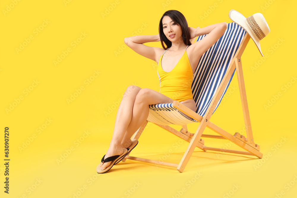 Beautiful Asian woman relaxing in deck chair on yellow background