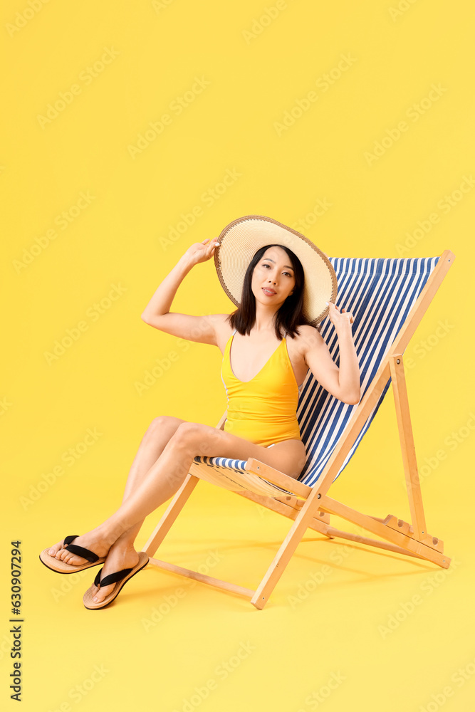 Beautiful Asian woman relaxing in deck chair on yellow background