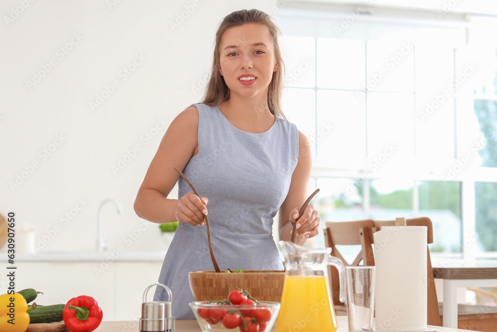 Young woman preparing vegetable salad in kitchen