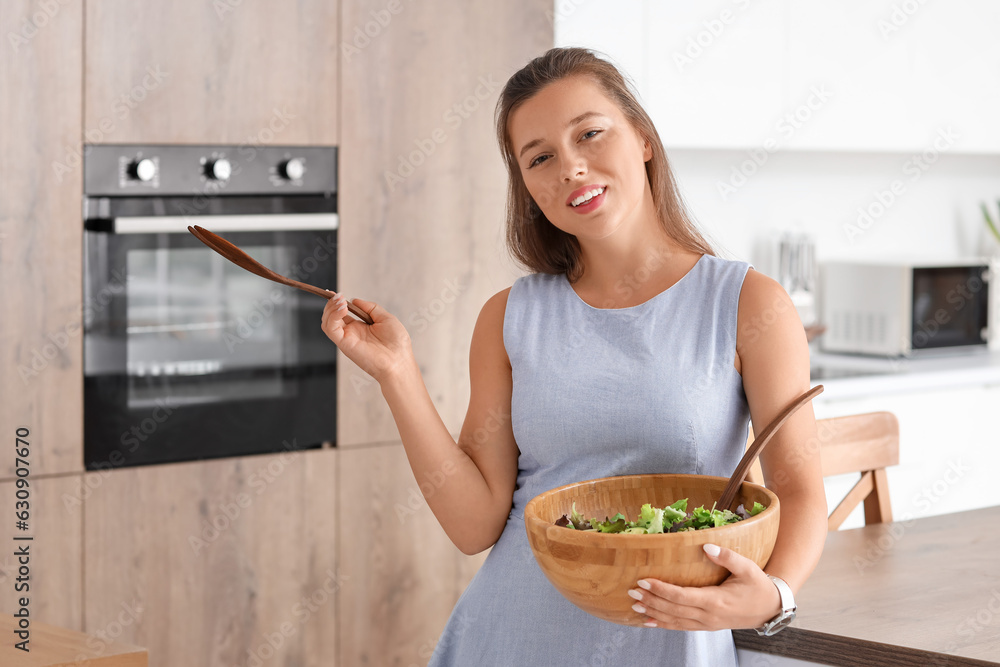 Young woman with bowl of vegetable salad in kitchen