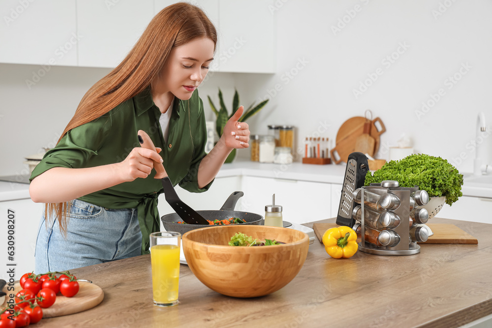 Young woman frying vegetables in kitchen