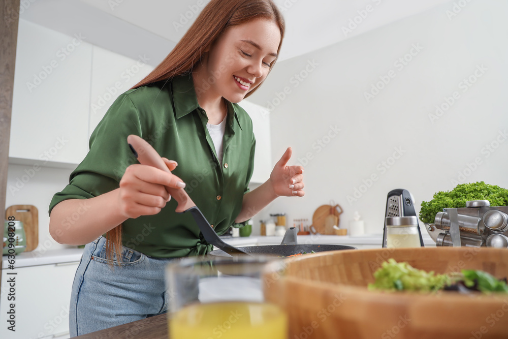 Young woman frying vegetables in kitchen