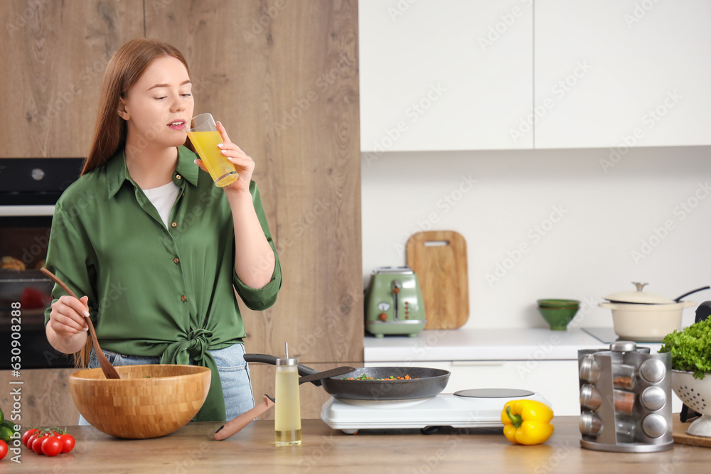 Young woman with vegetable salad and glass of juice in kitchen