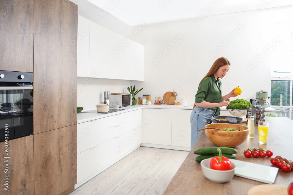 Young woman with fresh lettuce and bell pepper in kitchen