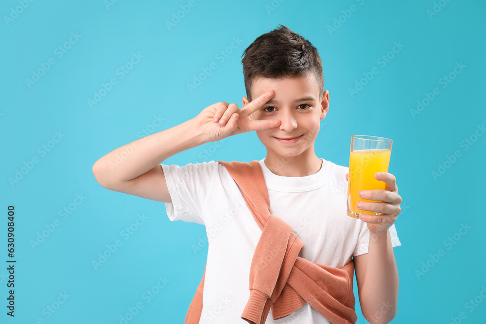 Little boy with glass of orange juice showing victory gesture on blue background