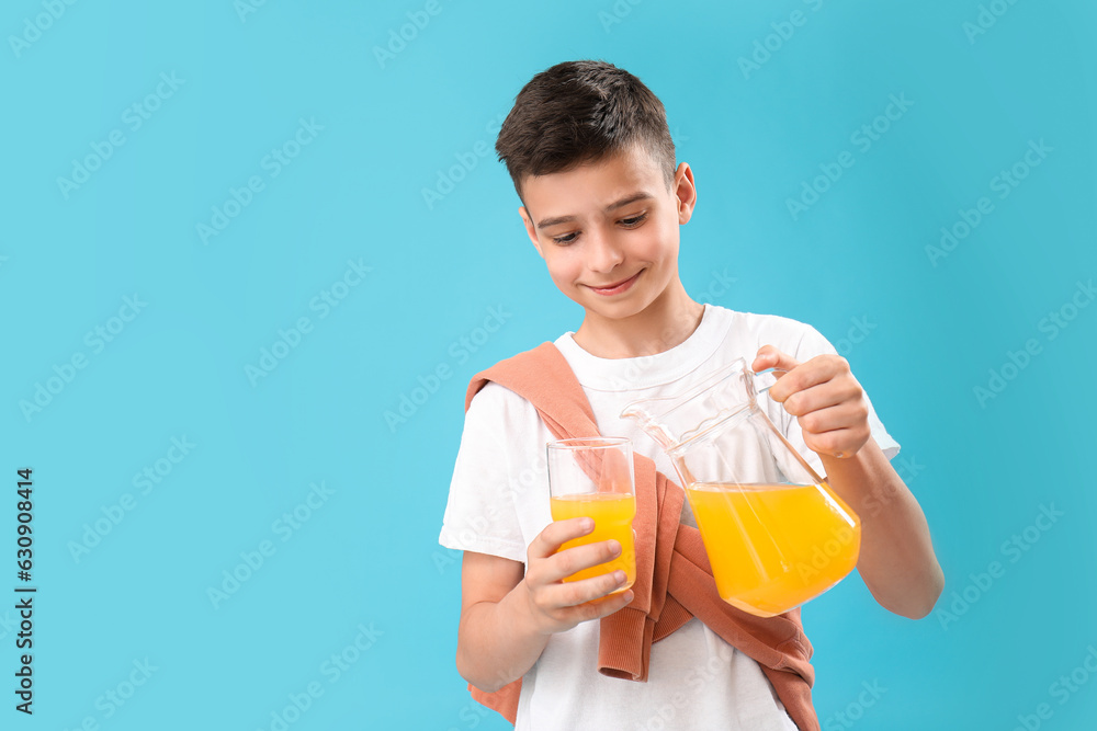 Little boy pouring orange juice into glass on blue background