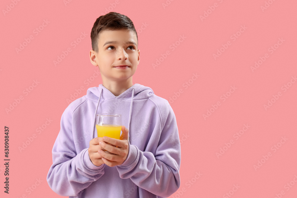 Little boy with glass of orange juice on pink background