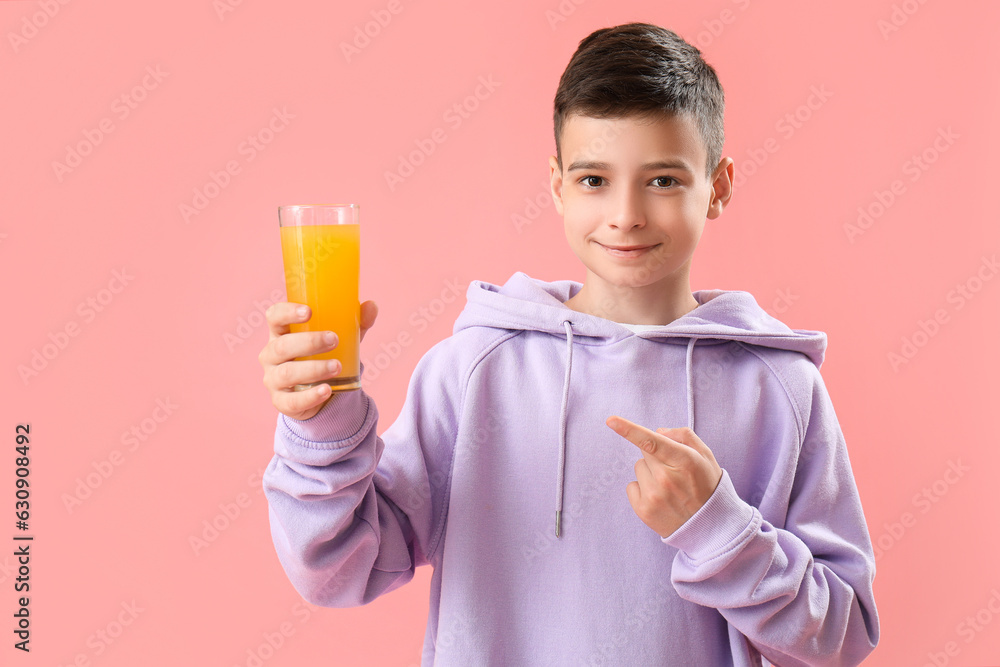 Little boy pointing at glass of orange juice on pink background