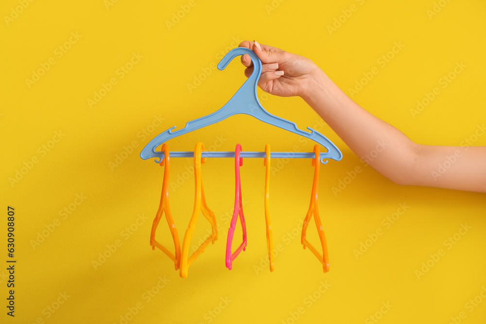 Woman holding plastic clothes hangers on yellow background