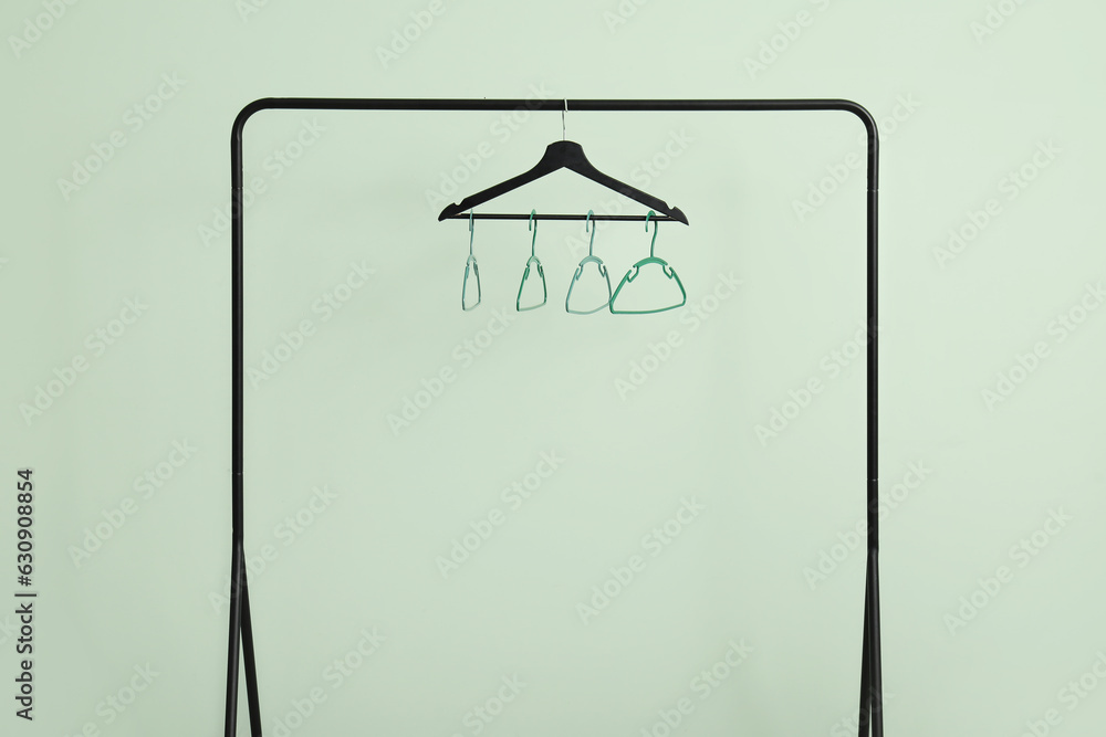 Rack with plastic clothes hangers on green background