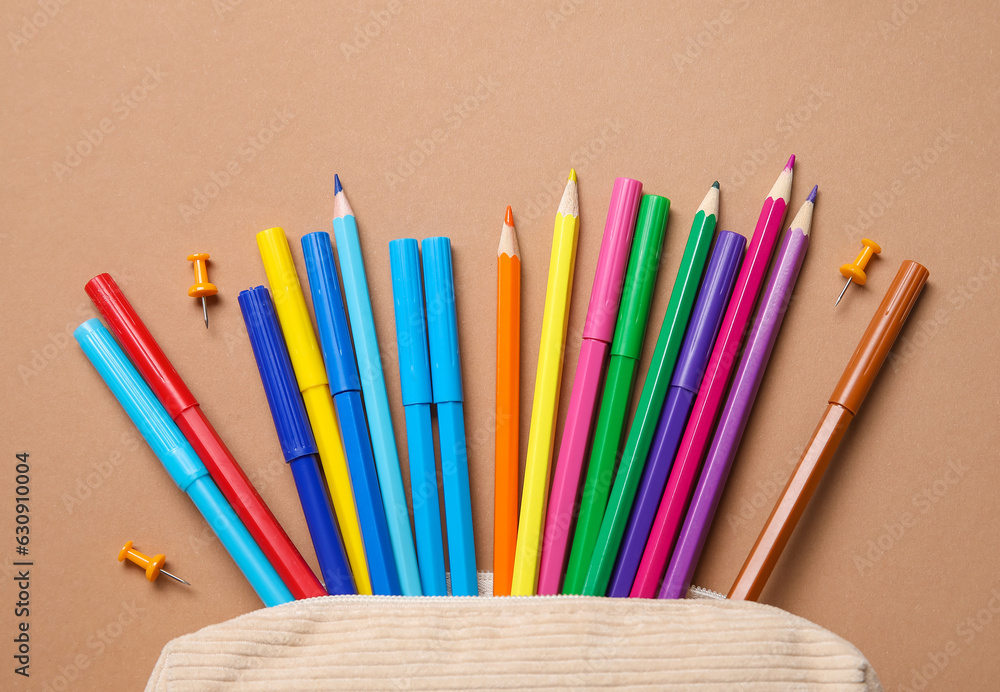 Pencil case with colorful markers, pencils and pins on beige background, closeup