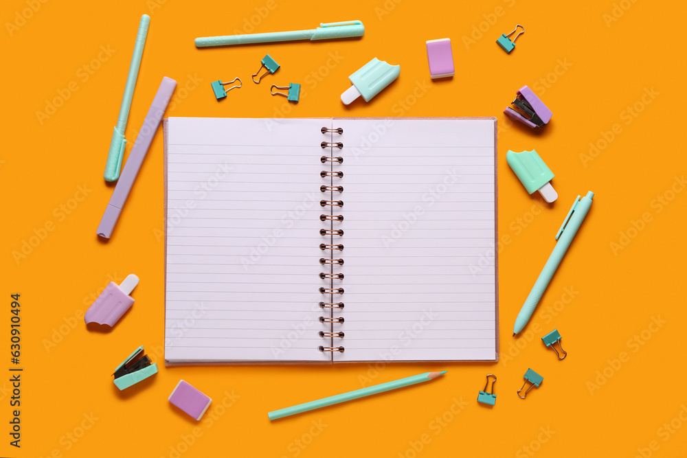 Notebook with different stationery supplies on orange background