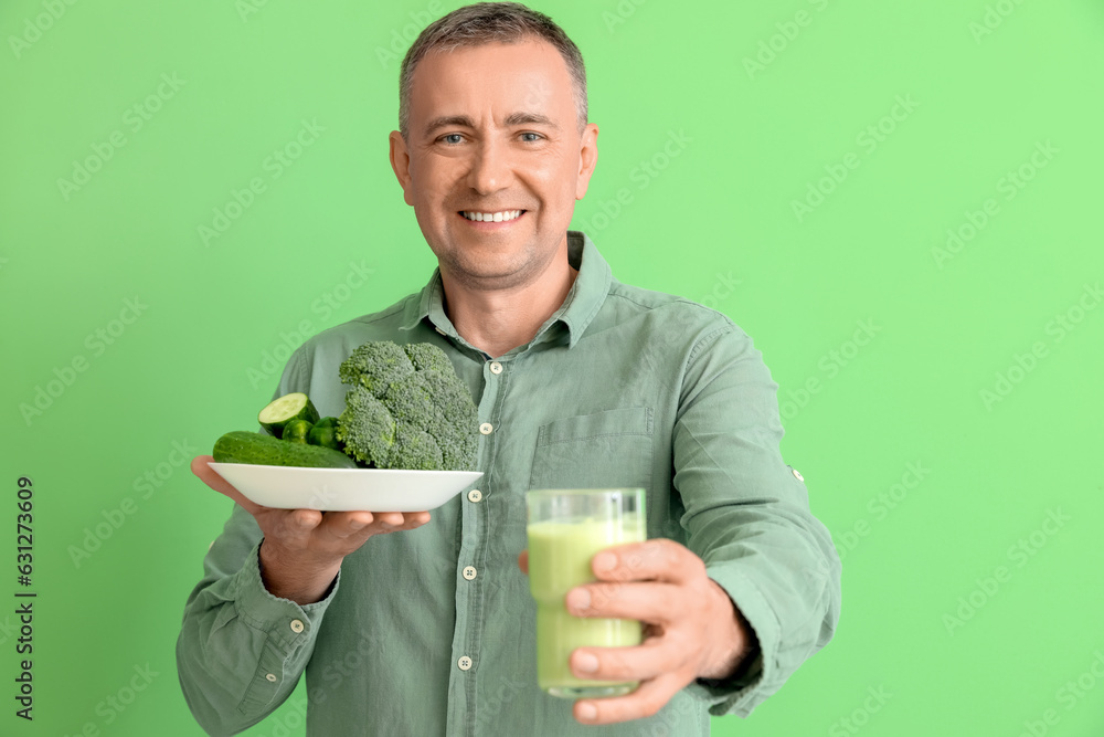 Mature man with glass of smoothie and vegetables on green background