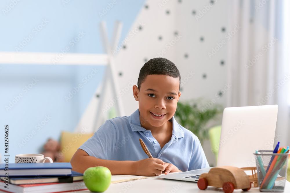 Little African-American boy studying computer sciences online in bedroom