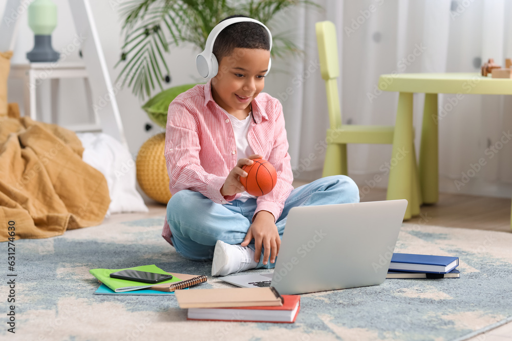 Little African-American boy with ball studying online in bedroom