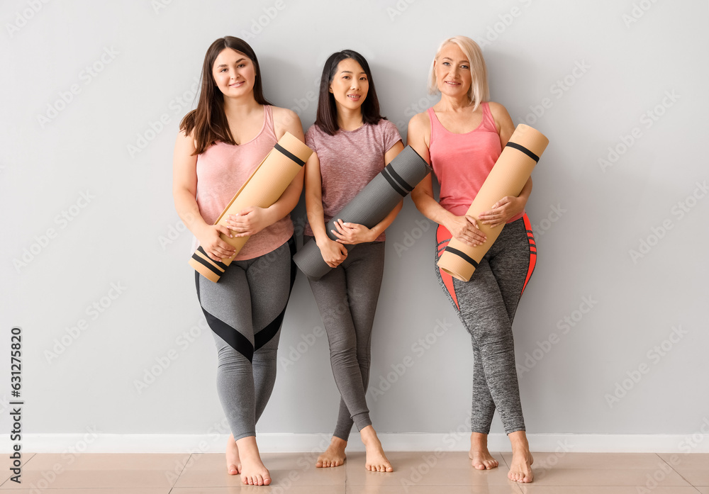 Sporty women with fitness mats near light wall