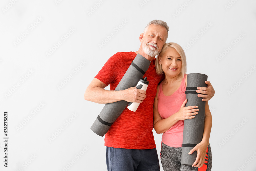 Sporty mature couple with fitness mats and water bottle on light background