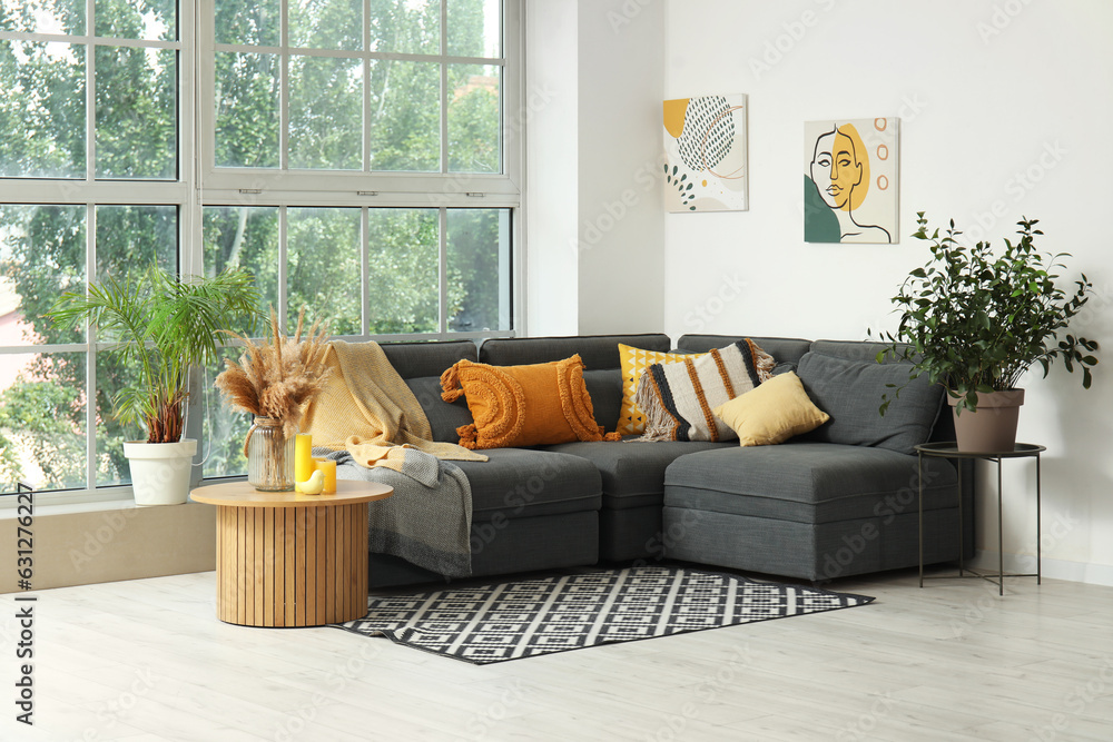 Interior of light living room with cozy grey sofa, coffee table and houseplants