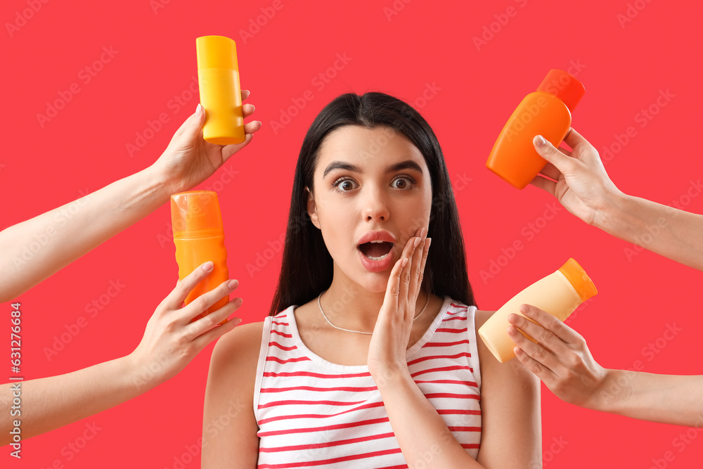 Surprised young woman and female hands with bottles of sunscreen cream on red background