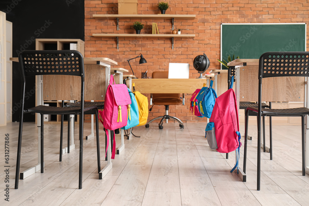 Interior of stylish empty classroom with backpacks and stationery