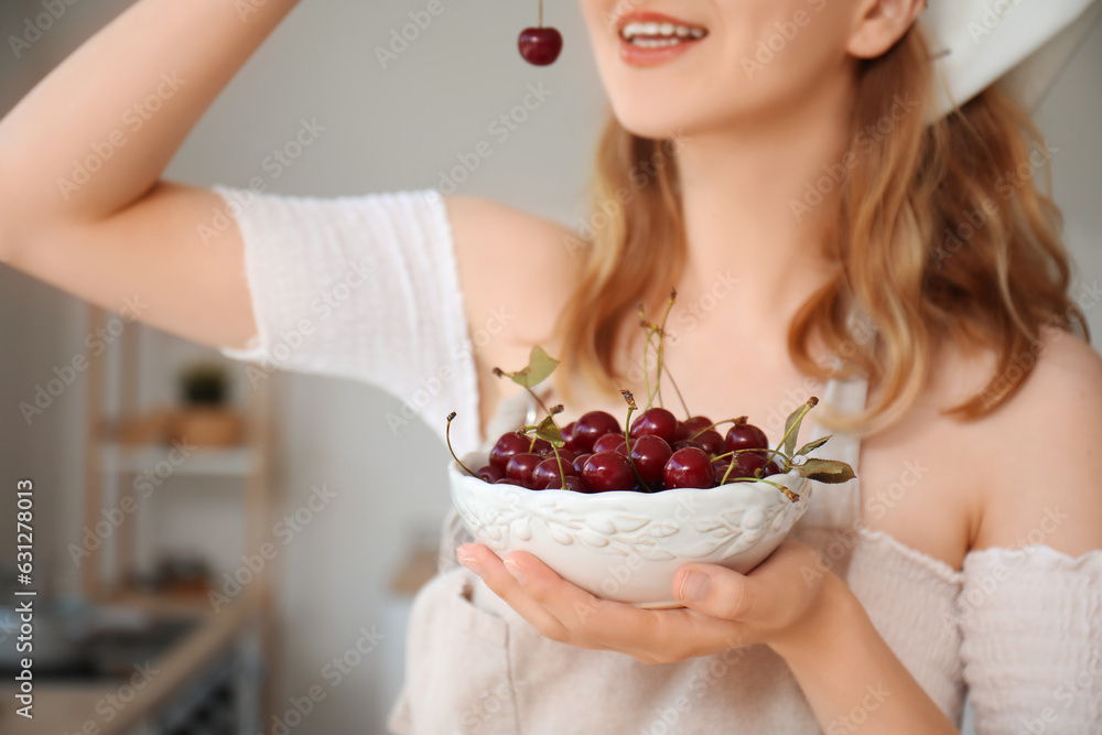 Beautiful happy young woman eating ripe cherries in kitchen