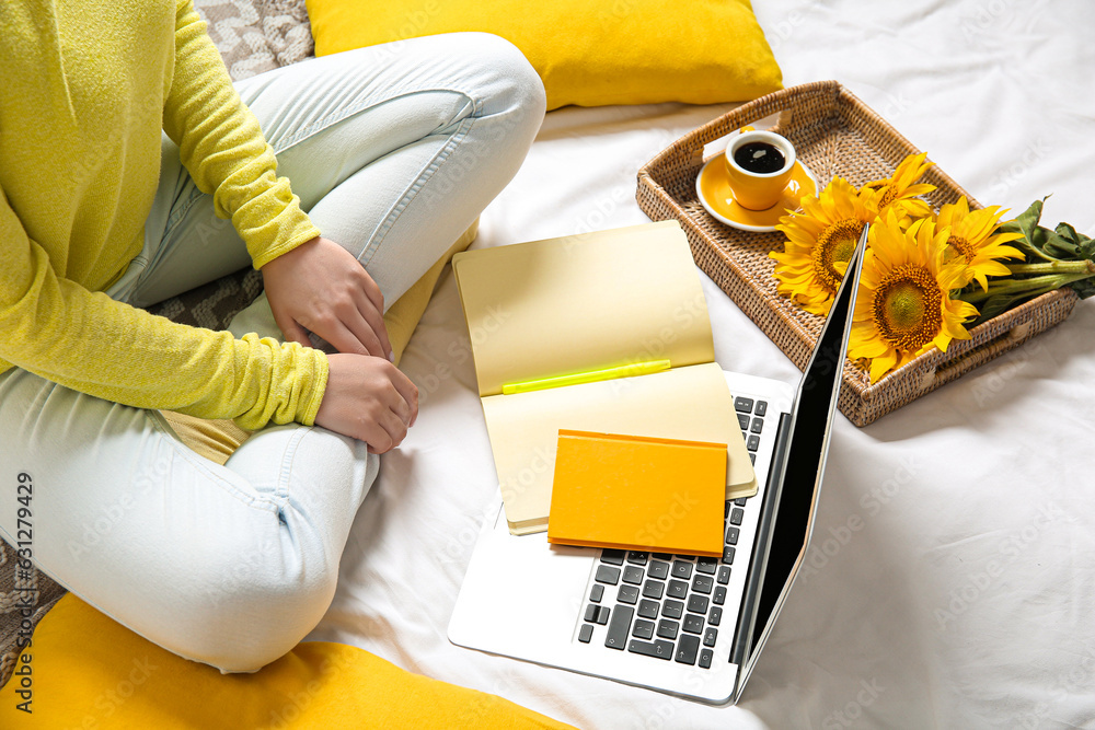 Woman with cup of coffee, laptop, sunflowers and notebooks in bed