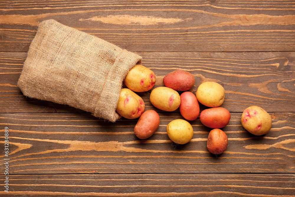 Sack bag with fresh raw potatoes on wooden background