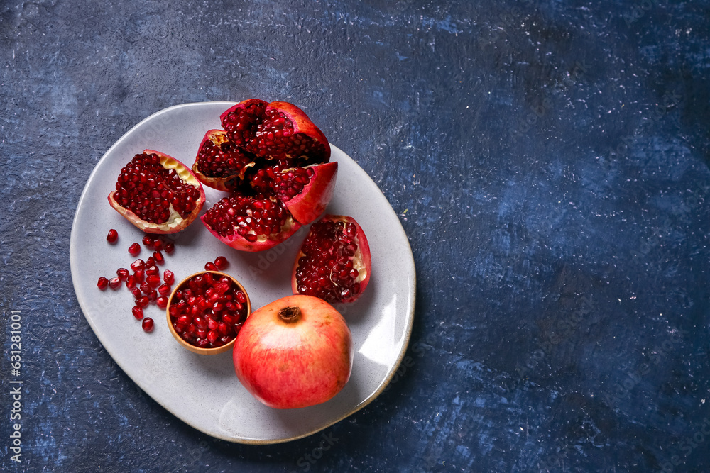 Plate with fresh pomegranates and bowl of seeds on blue background