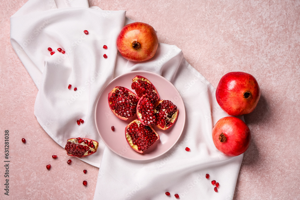 Plate with pieces of fresh pomegranate and seeds on pink background