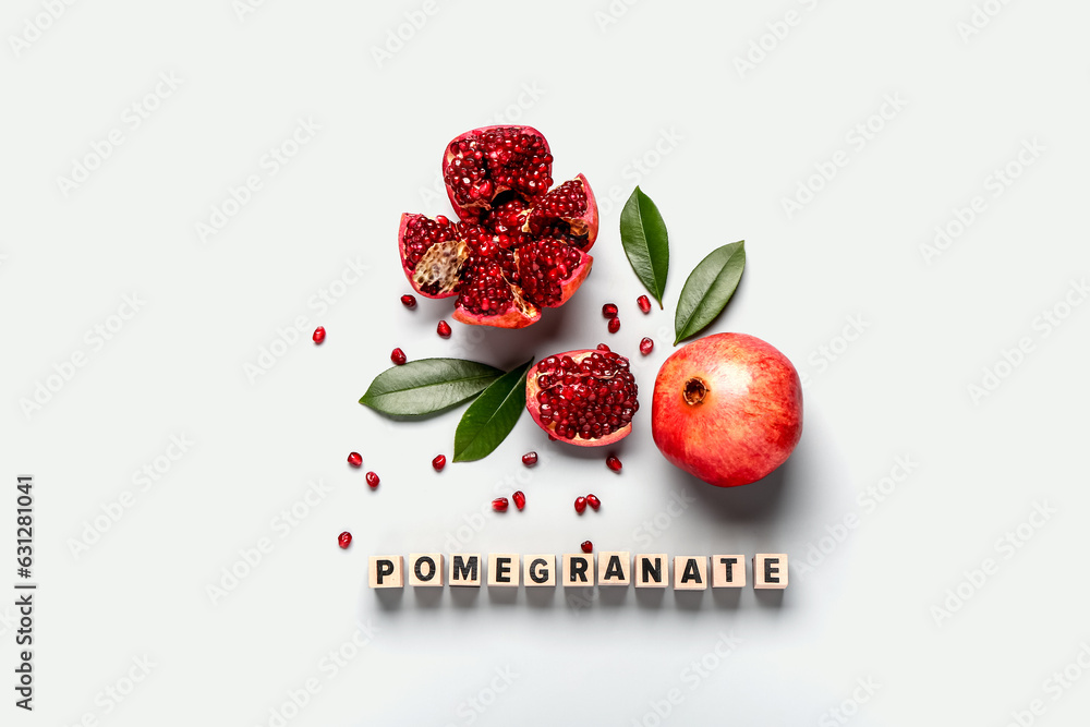 Word POMEGRANATE with fresh fruits and leaves on grey background