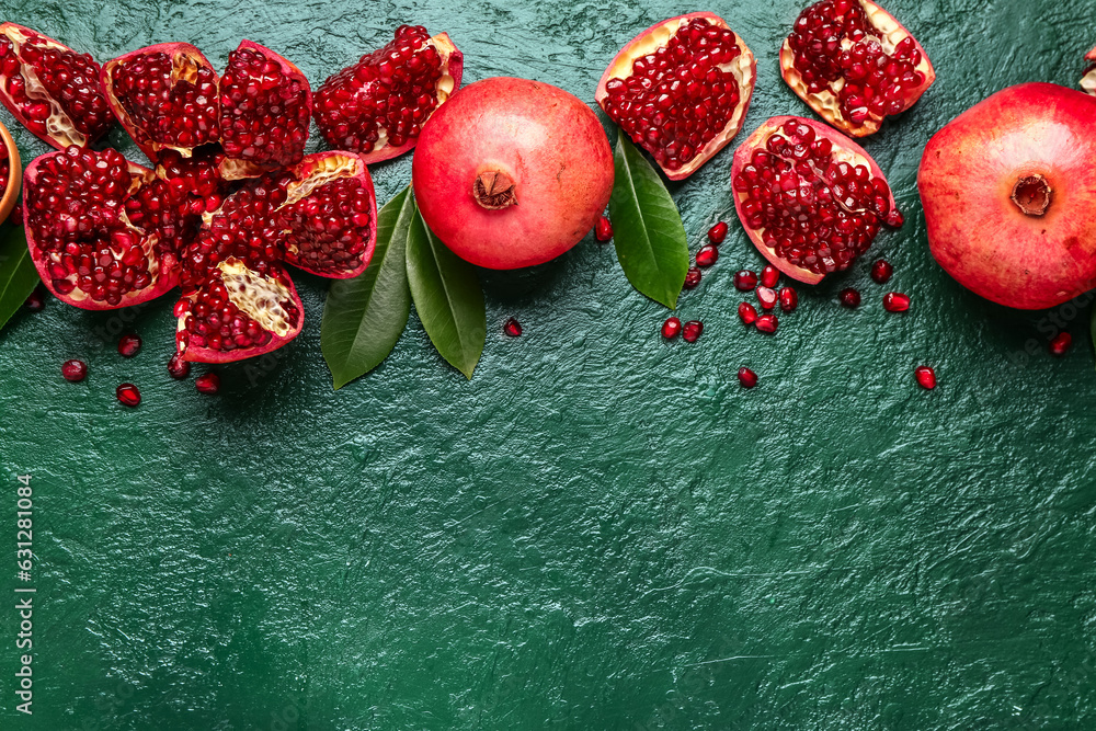 Fresh pomegranates with seeds and leaves on green background