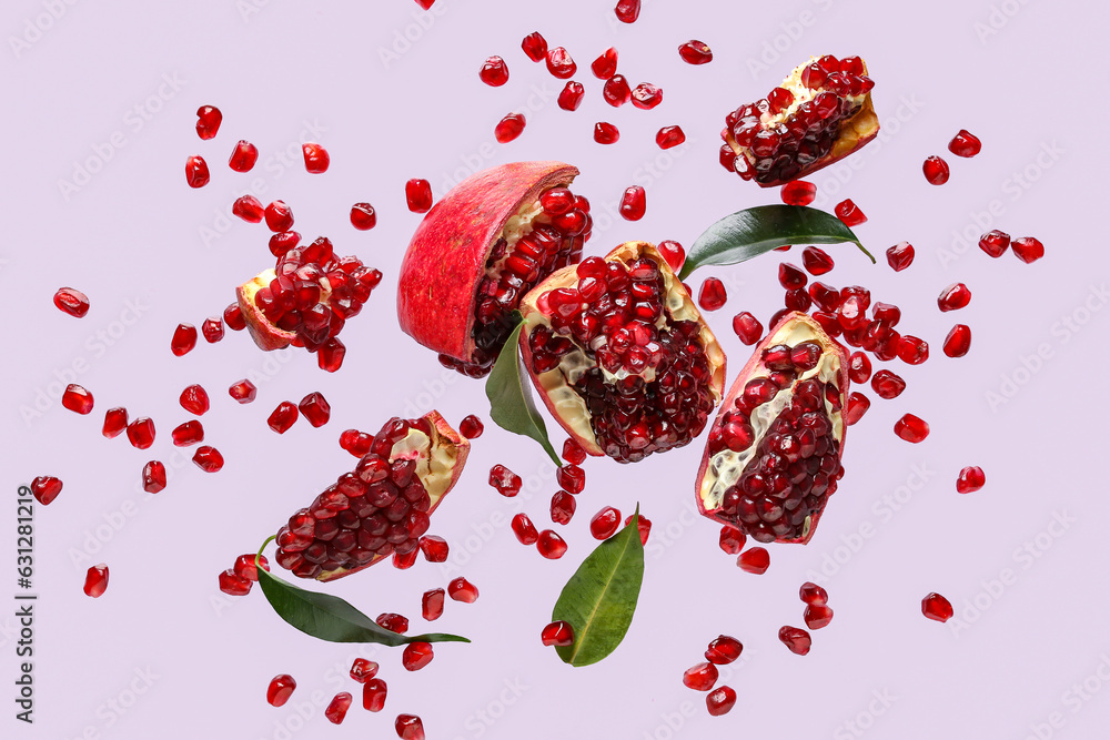 Flying fresh pomegranates with seeds and leaves on lilac background