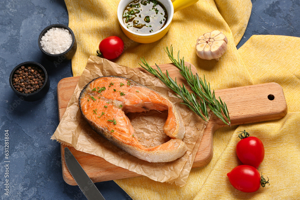 Wooden board of tasty salmon steak with tomatoes and spices on blue background