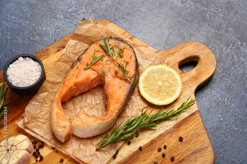 Wooden board of tasty salmon steak with lemon on blue background