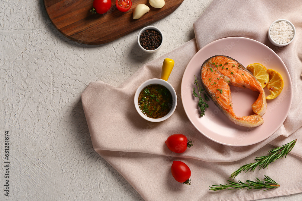 Plate of tasty salmon steak with tomatoes, sauce and lemon on grey background