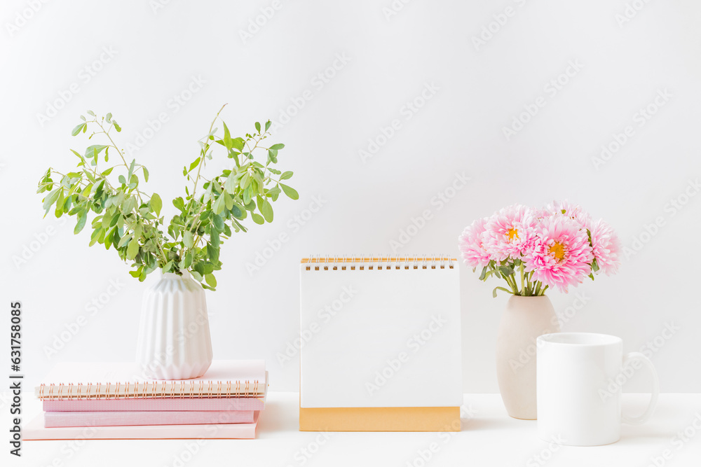 Mockup white desk calendar and pink flowers in a vase on a light background. Spiral calendar for moc