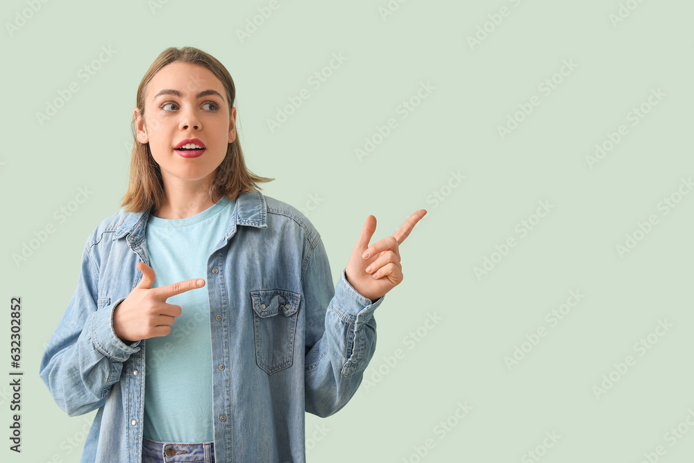 Young woman in denim shirt pointing at something on green background