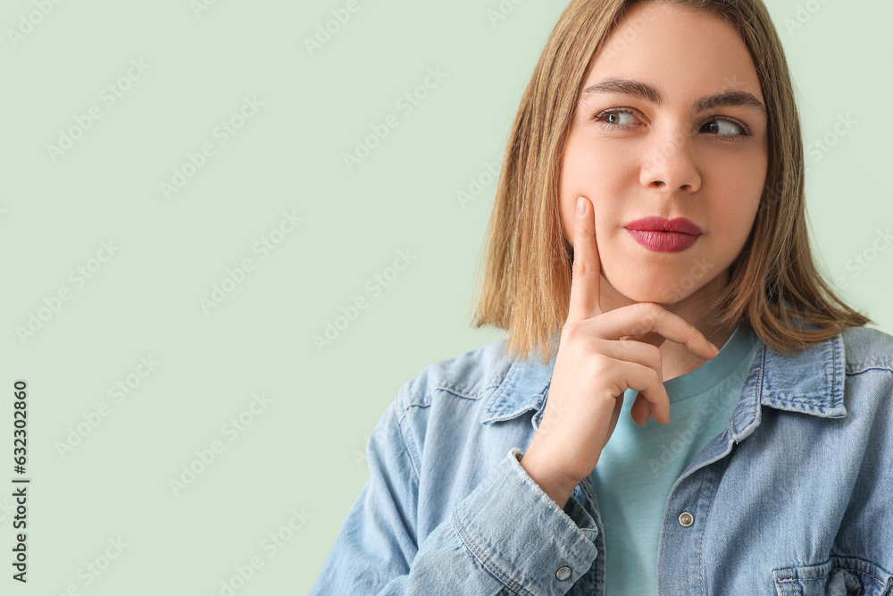 Thoughtful young woman in denim shirt on green background